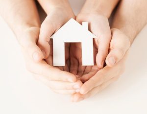 An adult’s and a child’s hands holding a paper cutout of a house.