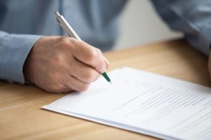 Closeup of a male hand holding a ballpoint pen poised over a Last Will and Testament for signature; selecting the appropriate types of wills.