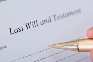 A hand holds a gold pen to sign a will. What does a will do? Wills can serve many purposes and provide several benefits.
